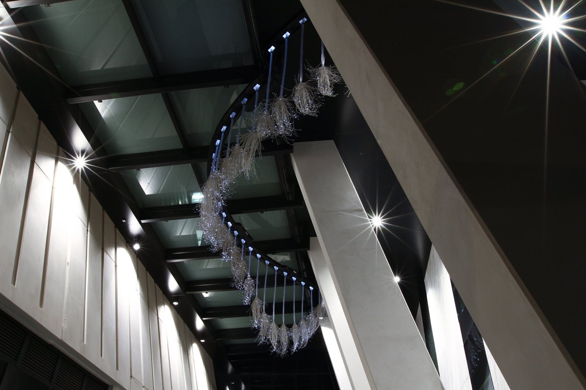 The installation curving down the length of the covered walkway, seen from below against the glazed ceiling