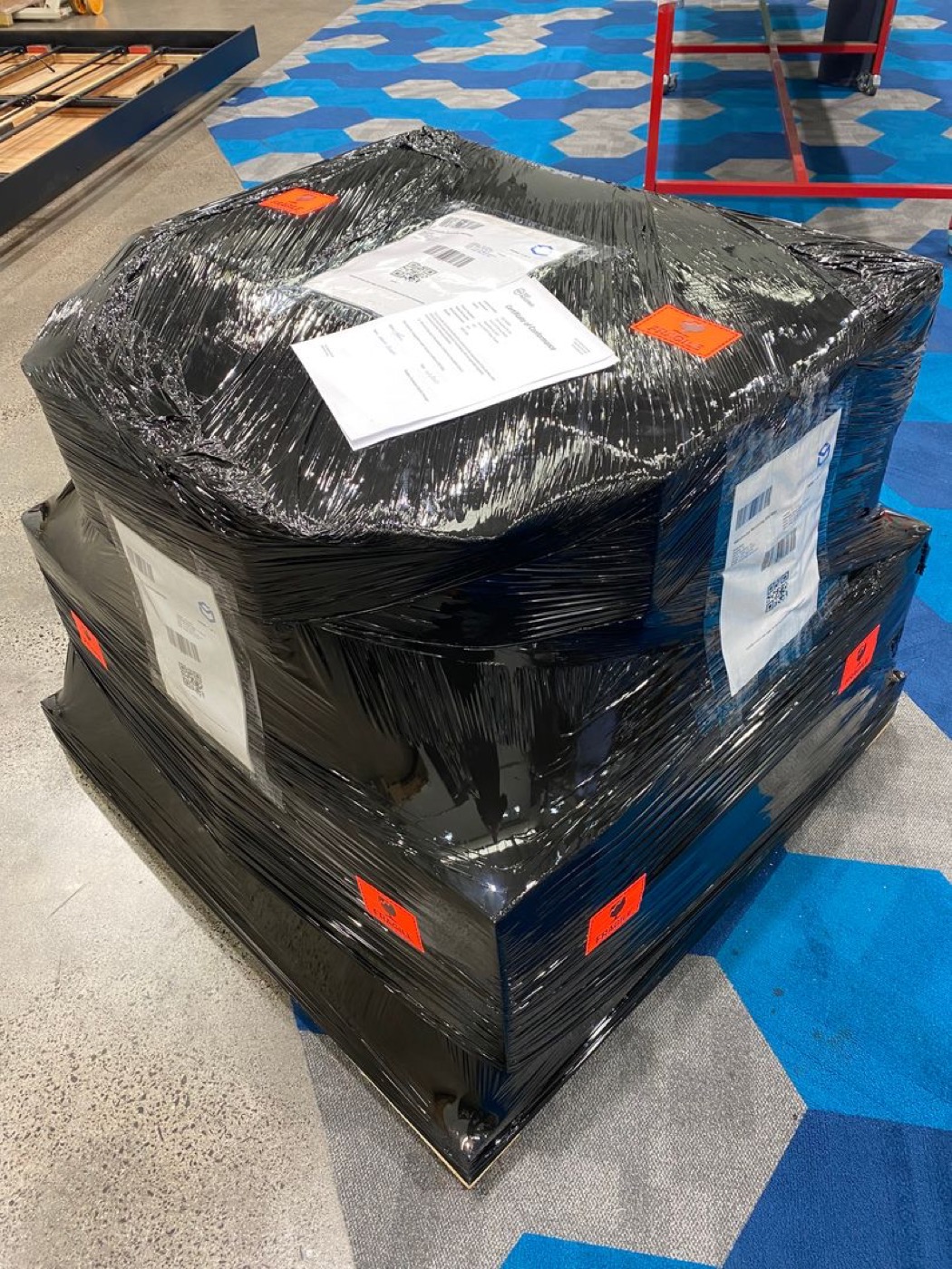 Export shipment of finished wearables shrink-wrapped in black film on a pallet, tagged with shipping labels and barcodes