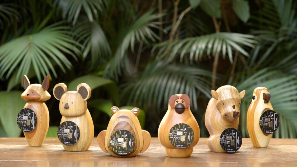 Six carved wooden animal figurines, each holding a round black Code of Conscience circuit board, tropical foliage behind