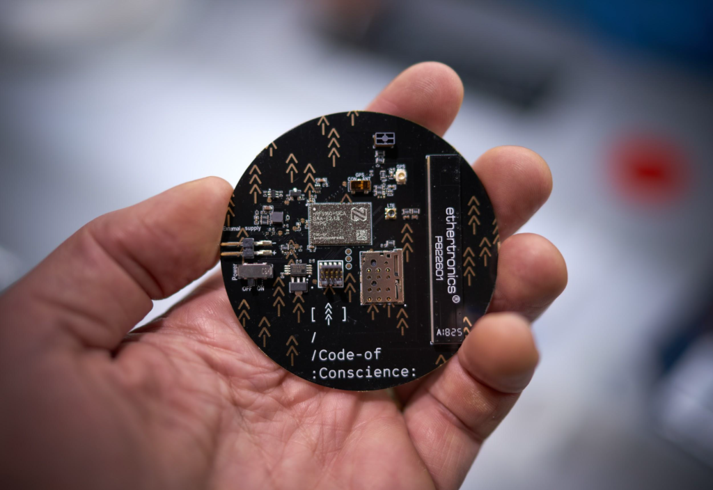 Hand holding the round Code of Conscience circuit board with nRF9160 module, antenna and tree-arrow motifs
