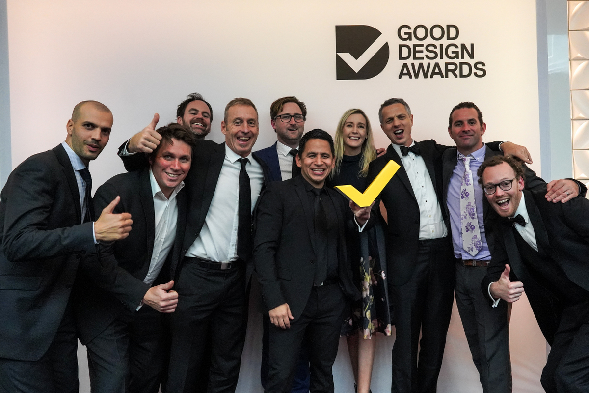 The Tekt and Fliteboard team in black tie at the 2019 Good Design Awards, crowded together with thumbs up around the yellow tick trophy beneath the Good Design Awards logo