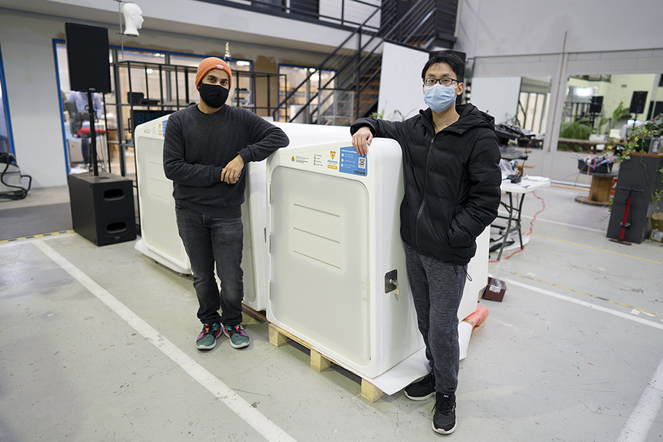 Two masked team members lean on white Petminda pods on timber pallets inside the manufacturing workshop