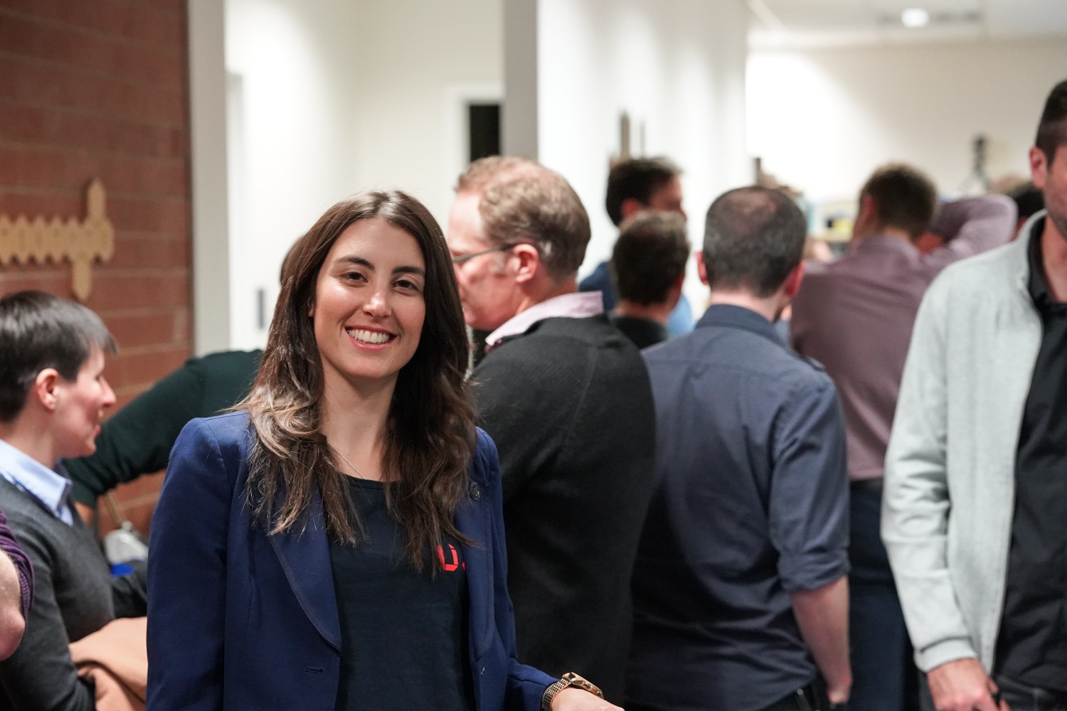A smiling guest in the foreground as attendees mingle through the office during the celebration