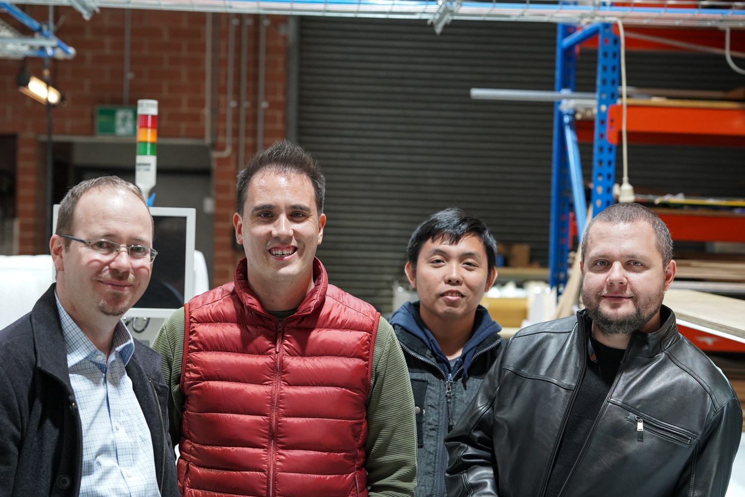 Four guests standing together in the workshop, with pallet racking and a roller door behind them