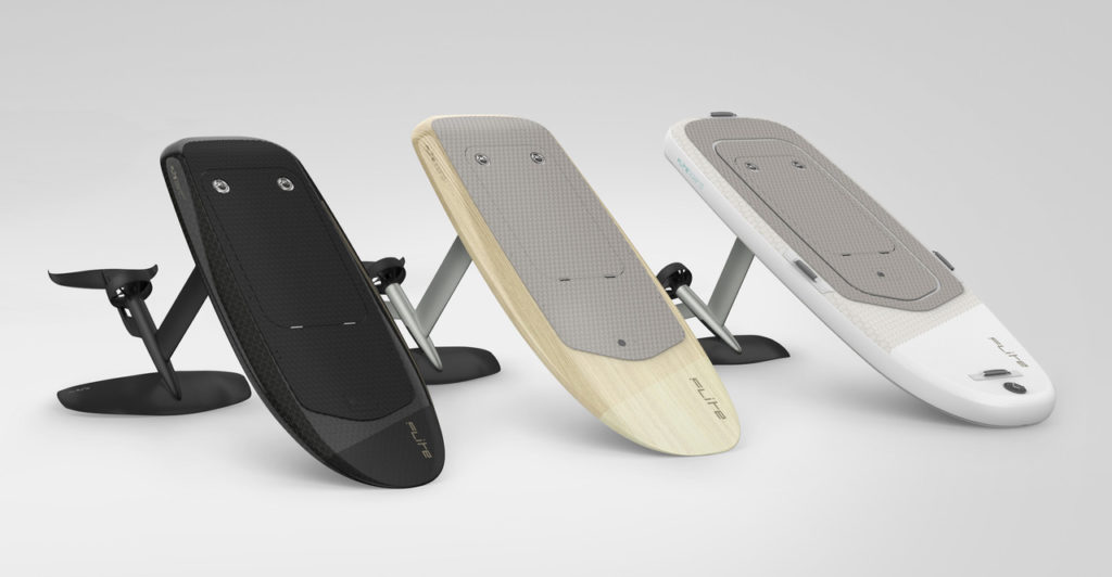 Three Fliteboard eFoils in black carbon, timber and white finishes, standing upright on their hydrofoil masts