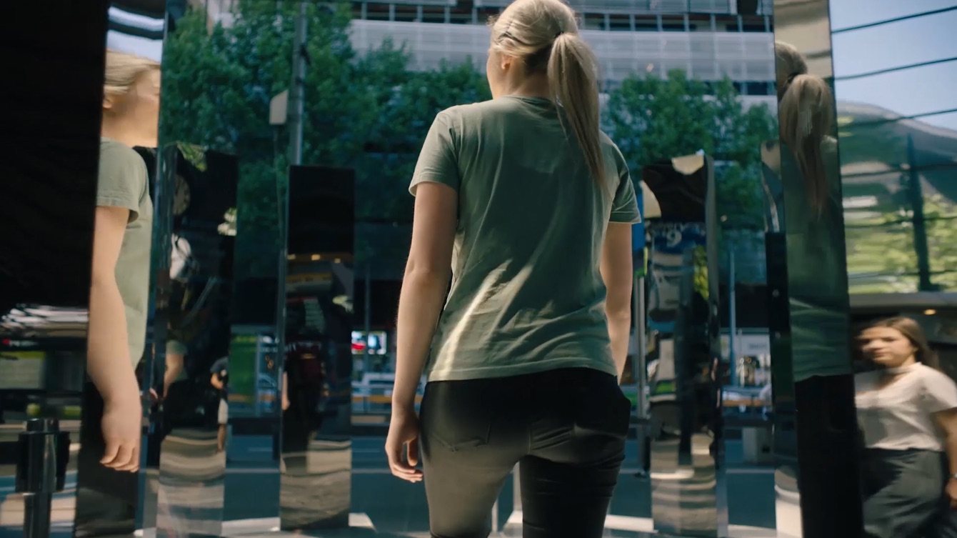 A visitor walks into the ring of mirrored columns at Southern Cross station, her reflection repeating across several