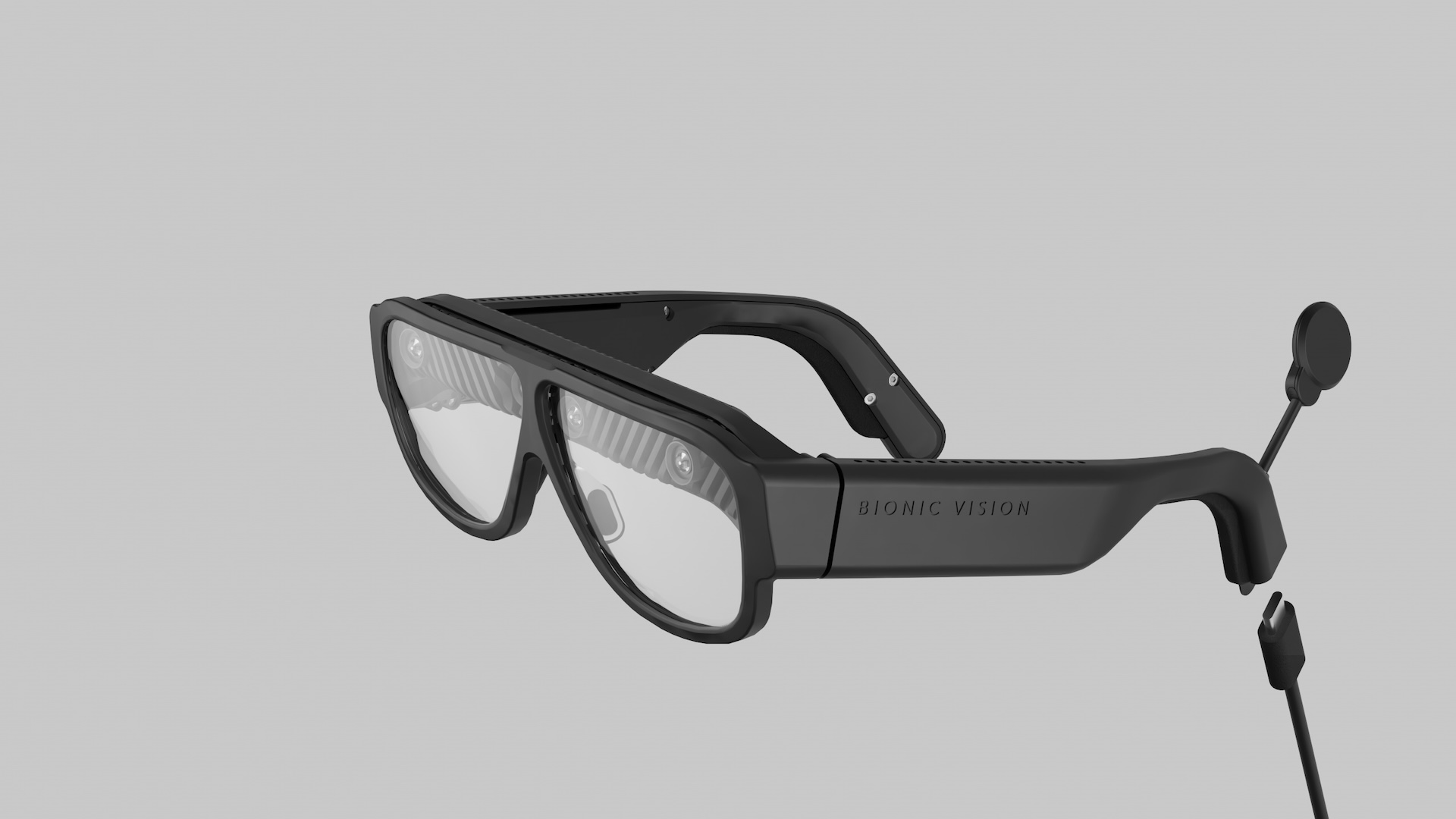 Three-quarter view of the glasses: sensor apertures behind the lenses, BIONIC VISION on the temple, coil on its stalk
