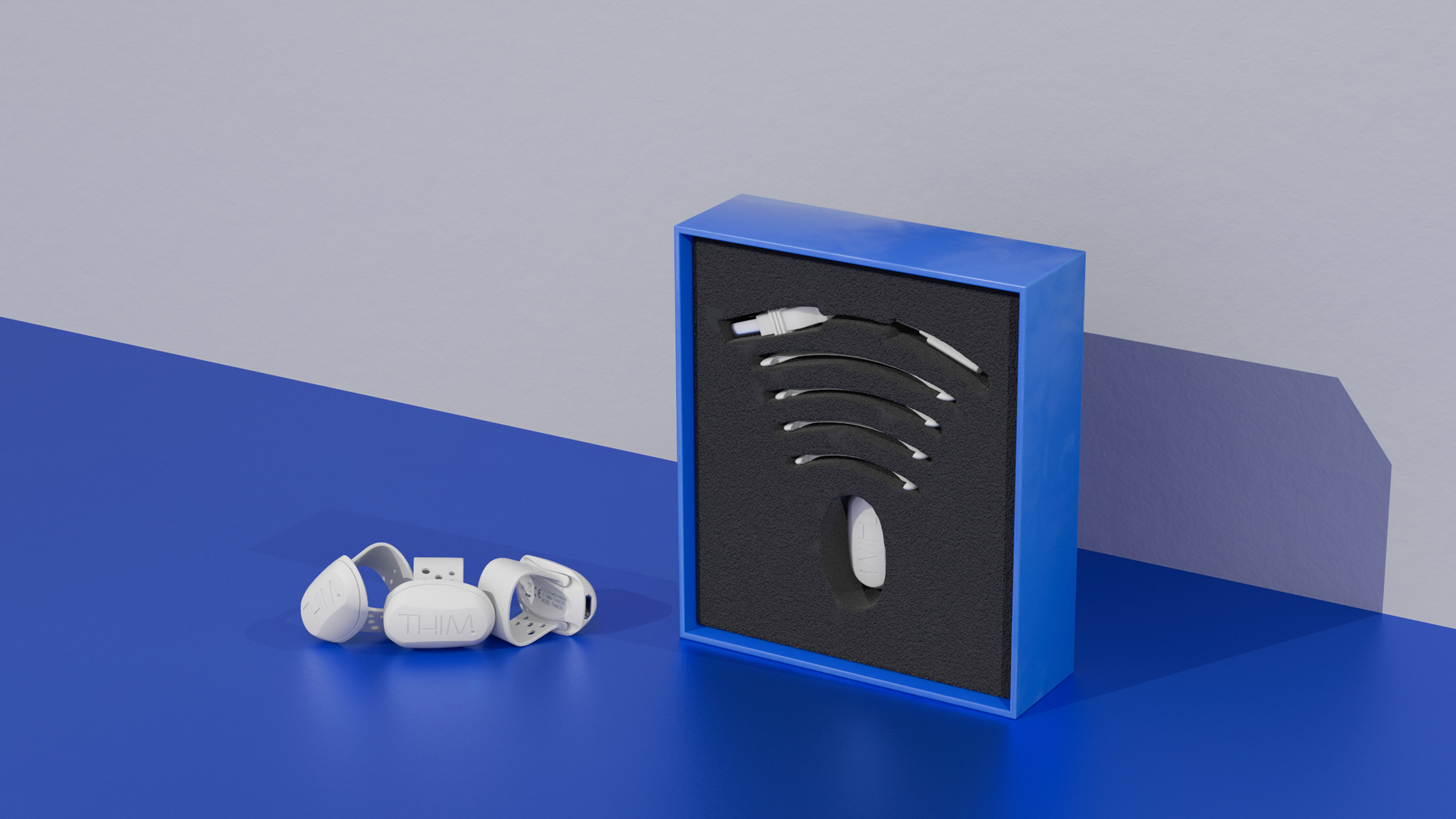 Angled view of the blue THIM box, its foam insert holding the wearable, straps and cable, with three units beside it